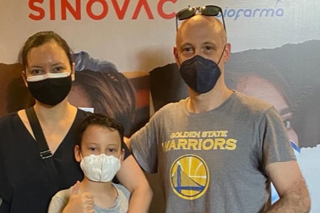 A mother and father stand either side of a young boy. All are wearing masks.