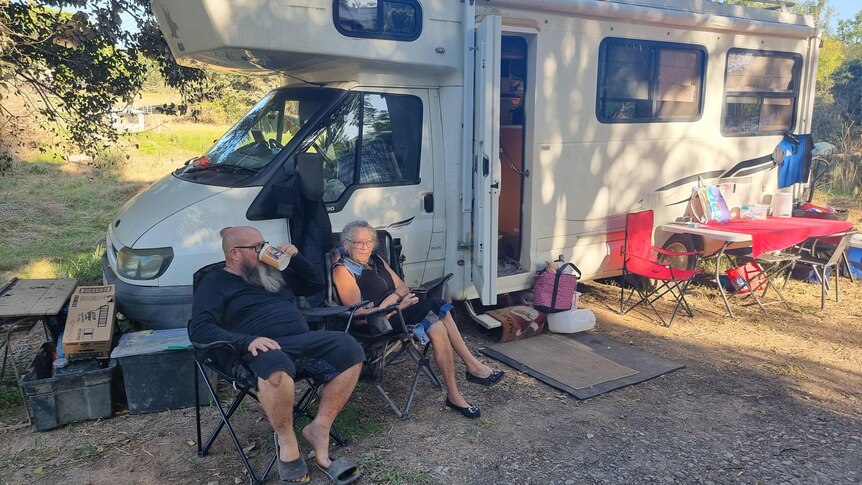 man and woman sit outside an RV on camper chairs