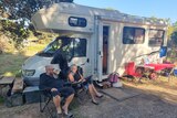 man and woman sit outside an RV on camper chairs