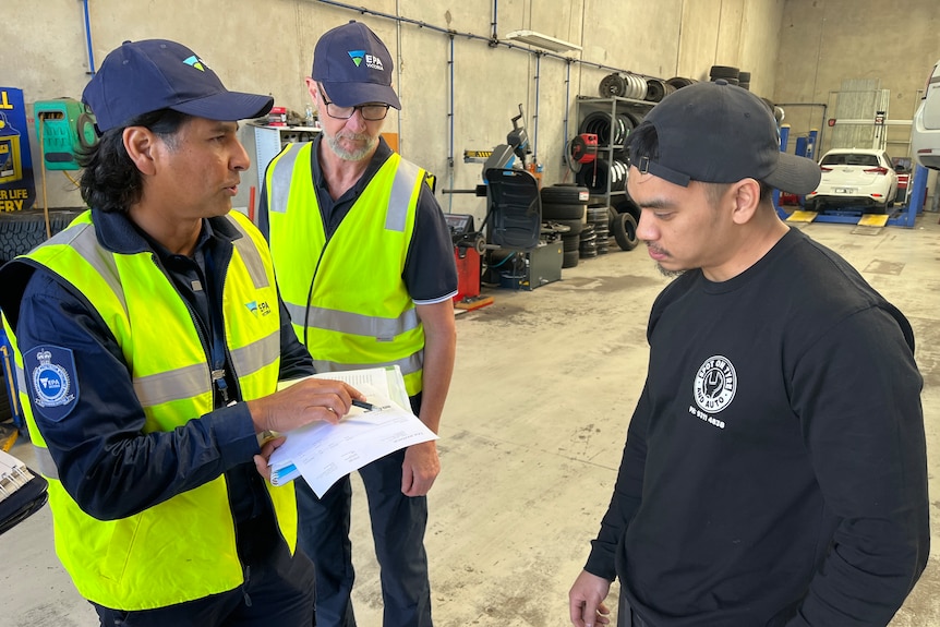 EPA Victoria officers in high-vis speaking to a man in a garage.