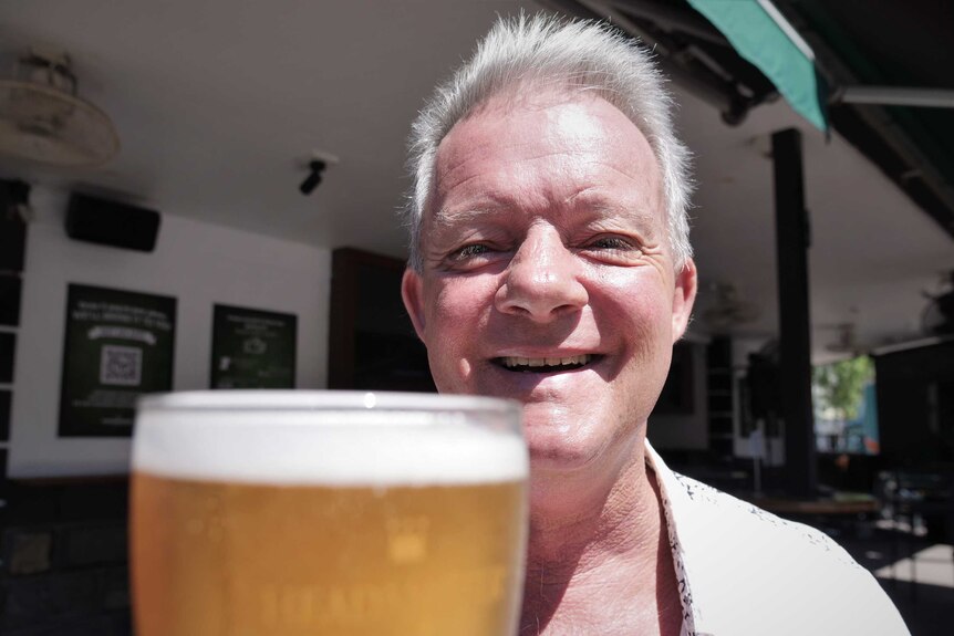 Bruce Masters holds out a beer with a big smile.