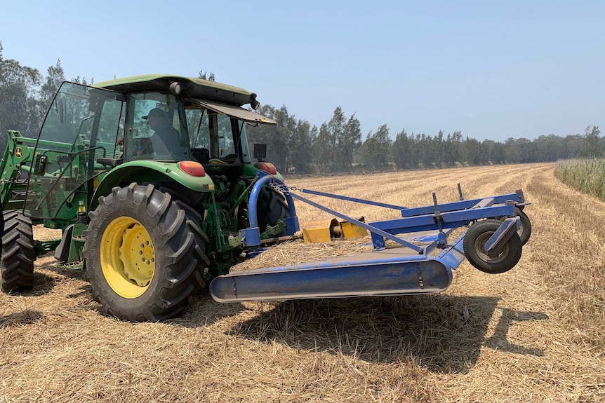 A man drives a tractor on a dirt road on a rural property.