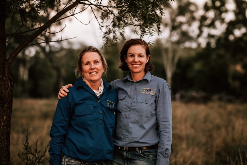 Two woman stand on a rural property with their arms around each other