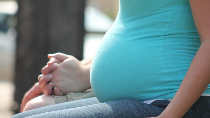 the image shows a pregnant woman's belly as she sits outside in sunlight