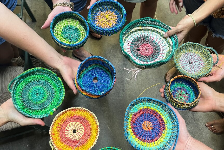 People hold out colourful woven baskets.