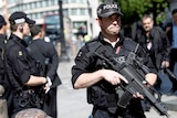 Armed police officers stand on duty outside St Paul's Cathedral in London, one holds a large gun.
