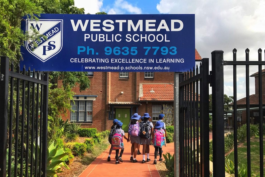 The Westmead Public School sign on top of a black fence with school children walking in the background.