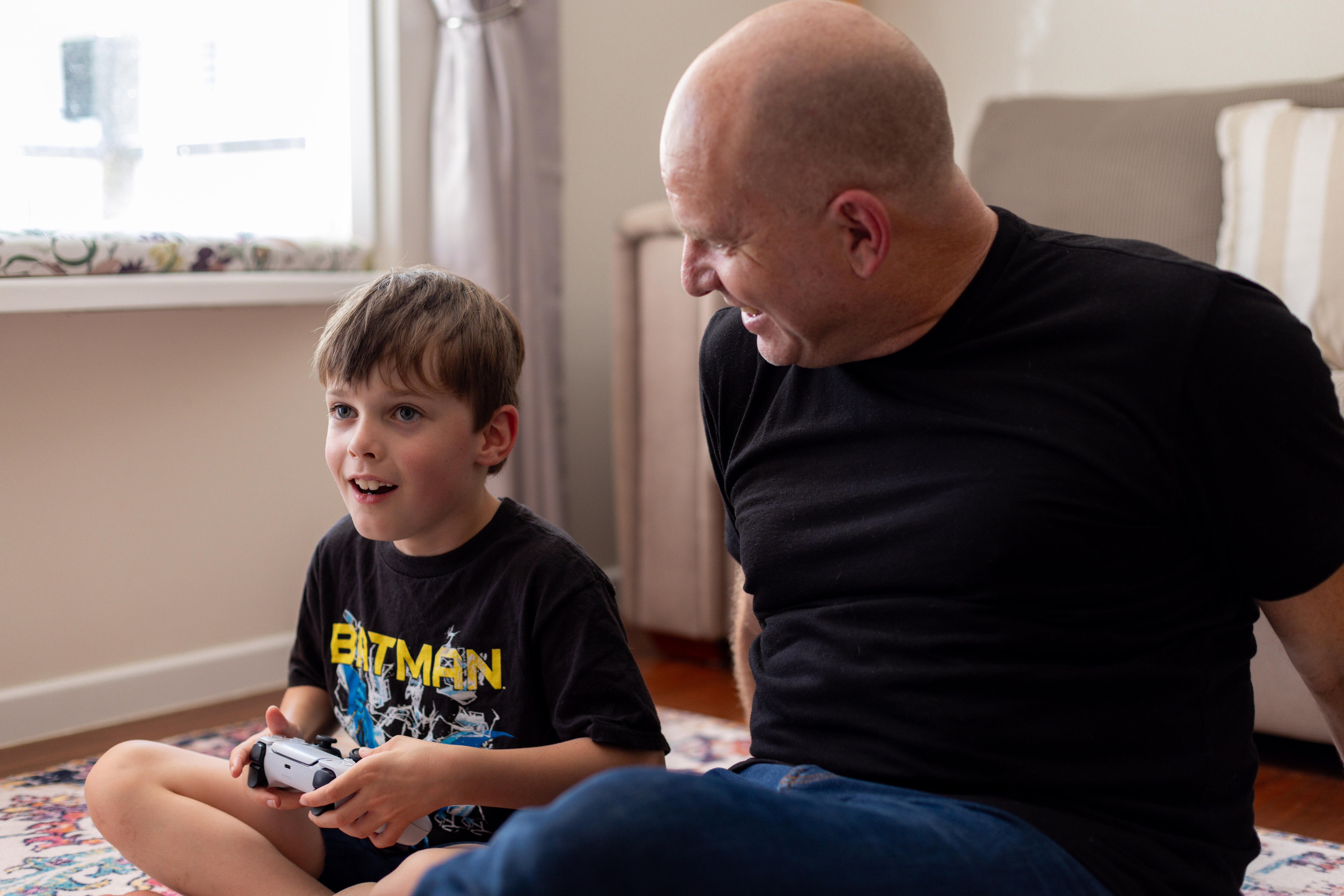 A man and boy holding game controller sitting on the floor 