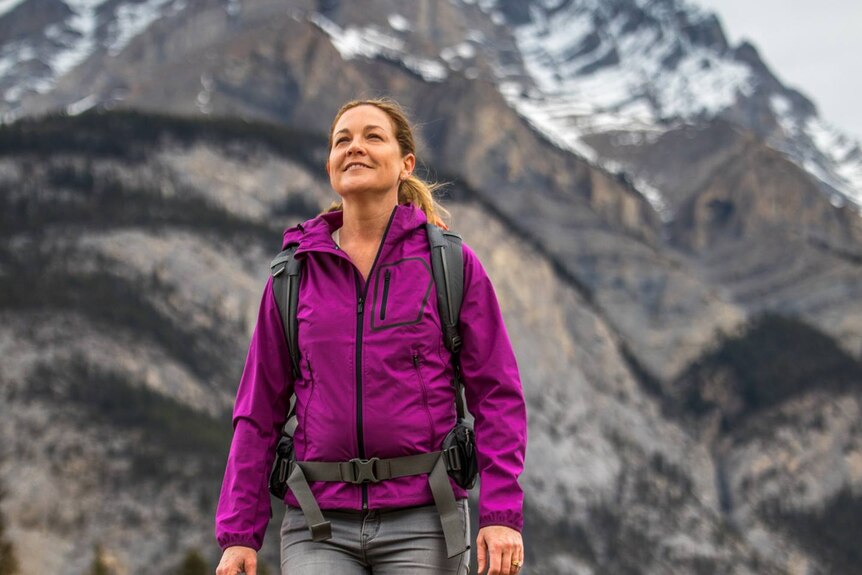 A woman in a pink jacket and hiking gear with a mountain in the background.