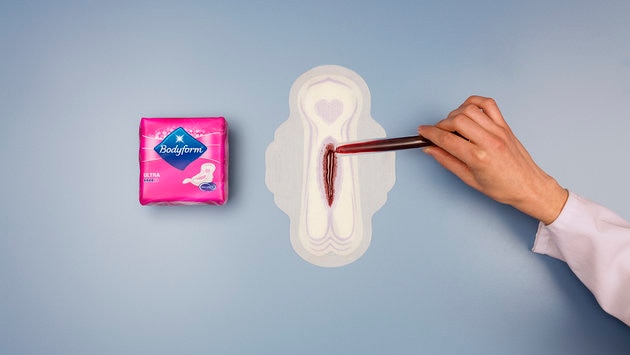 Test tube of blood being poured onto menstrual pad.