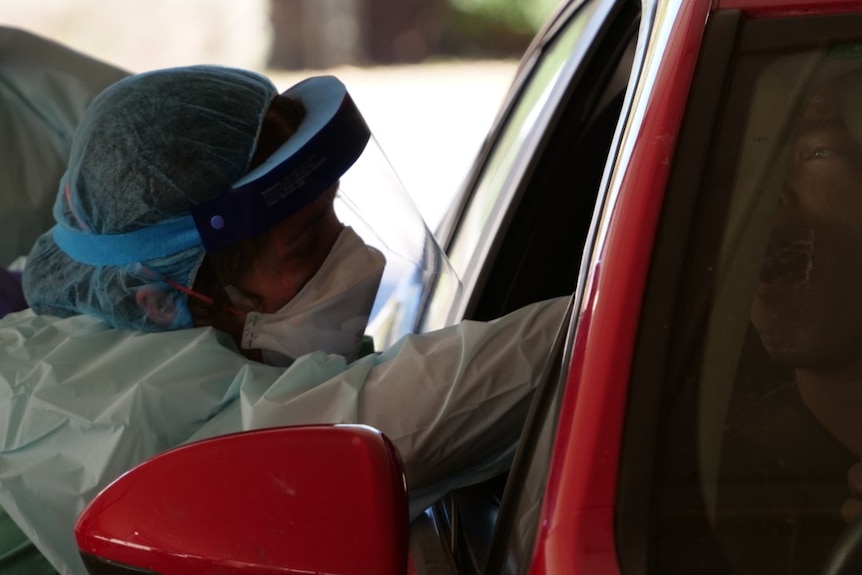 Medical profession taking a mouth swab test from a person in their car to test them for coronavirus