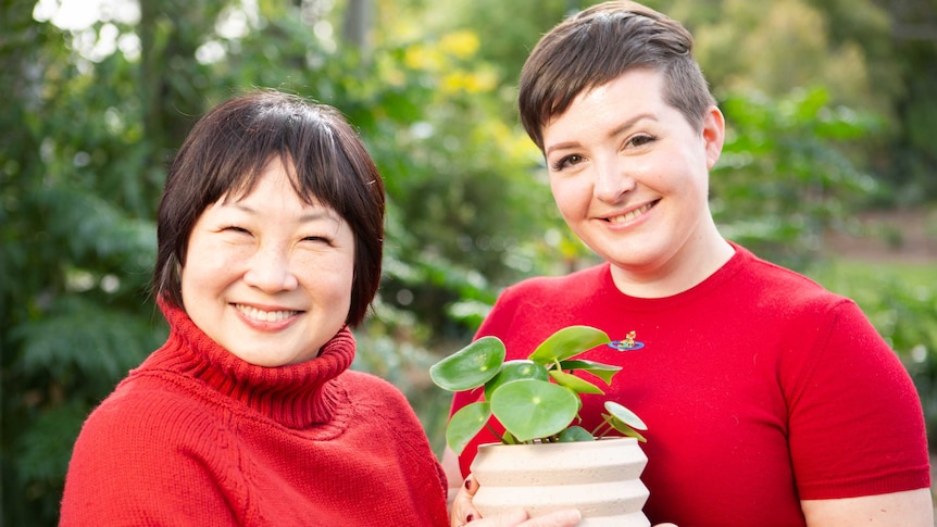 'Kinder World' mobile game app developers Christina Chen and Lauren Clinnick pose in a garden setting holding a pot plant.