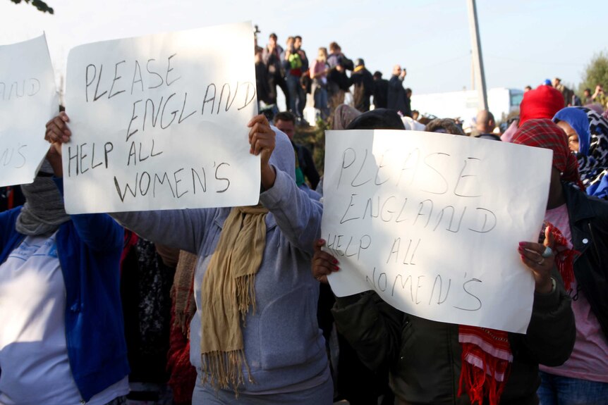 Women hold signs reading "please England help all women's"