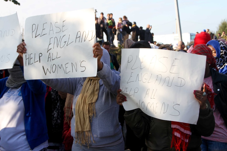 Women hold signs reading "please England help all women's"