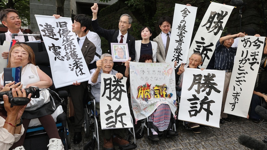 A group of Japanese citizens holding up banners in celebration after a court ruling