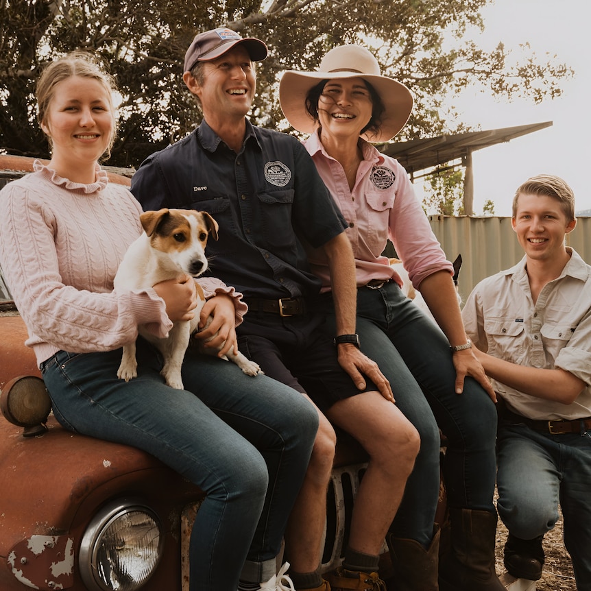 A family posed with a dog on the bonnet of an old rusty truck.