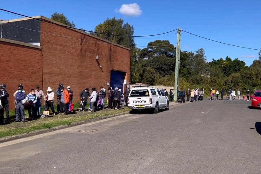 People stand in a long queue outside a brick warehouse