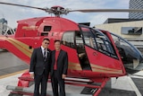 Ming Xu and Hongqing Zhu stand in front of a red helicopter.