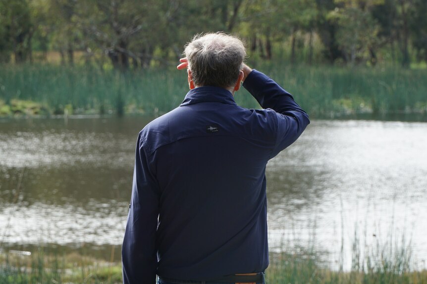 一名男子背对镜头，眺望克莱蒙特湖，用右手遮住眼睛。