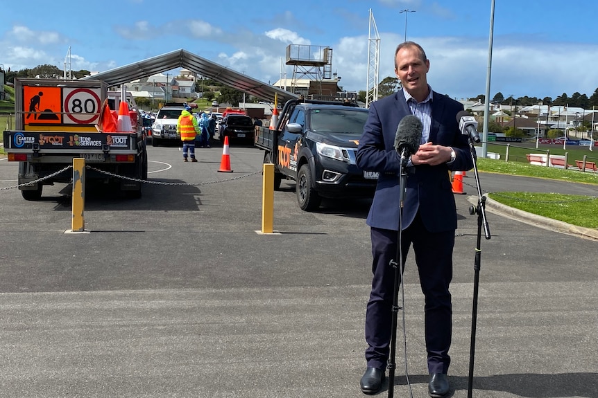 Man in suit at press conference with covid test site behind