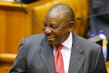 Cyril Ramaphosa smiles while holding his glasses in Parliament.