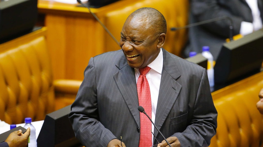 Cyril Ramaphosa smiles while holding his glasses in Parliament.