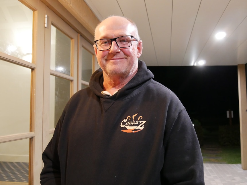 a man smiles at the camera, wearing a hoodie and glasses
