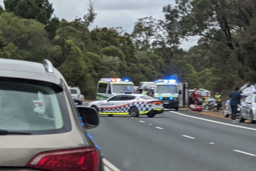 A car crash scene with two ambulances and police cars on the side of the road.
