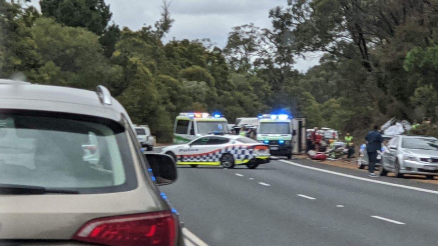 A car crash scene with two ambulances and police cars on the side of the road.