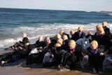 People in Trump masks and suits spilling off plastic chairs and into the ocean.