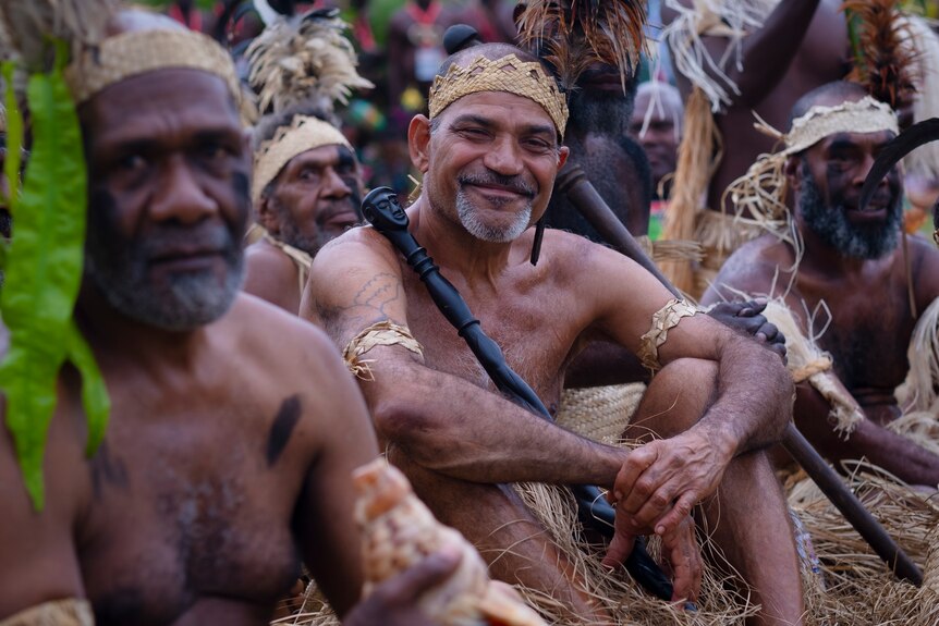 Melanesian cultural performer smiles holding a black club wearing a woven crown