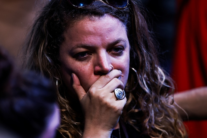 A close up of a woman with her hands on her mouth with tears in her eyes.