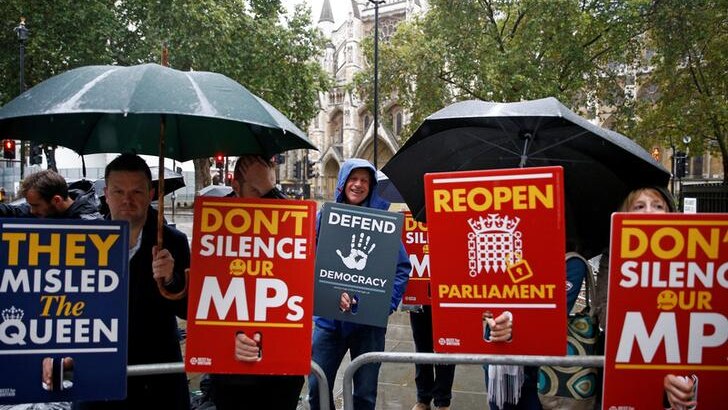 Protesters hold signs calling for Parliament to be reopened and for MPs to be unsilenced outside court.