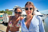 Two young women of Latin American background standing in front of a boat on a sunny day