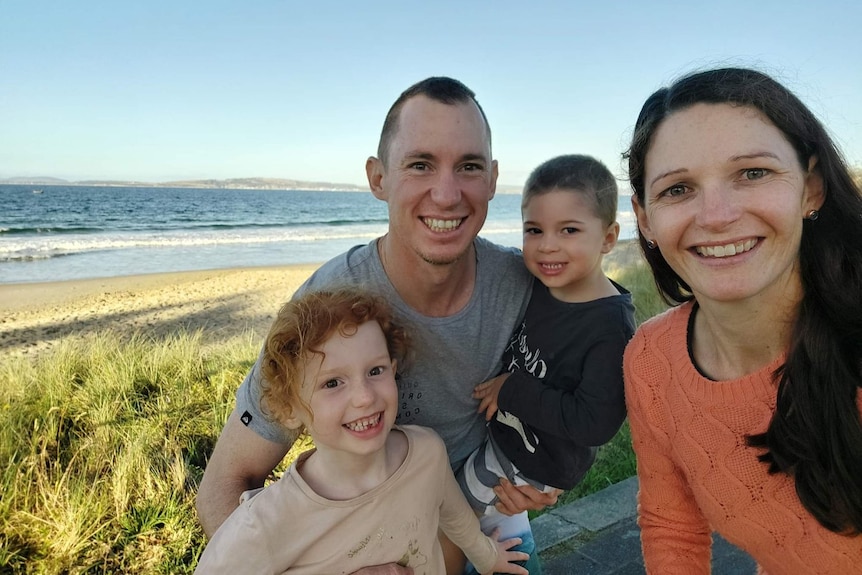 A smiling young family of four at a beach.