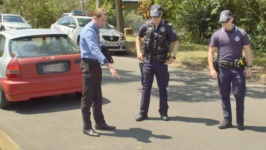 A detective points to paint spots on the road at Tarragindi where a man was hit by a car.
