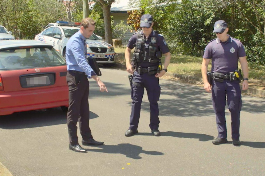 A detective points to paint spots on the road at Tarragindi where a man was hit by a car.