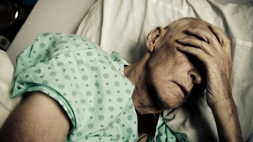 Sick man wearing hospitable gown lying in bed