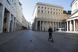 A man wearing a mask rides a scooter through an empty street in Milan.