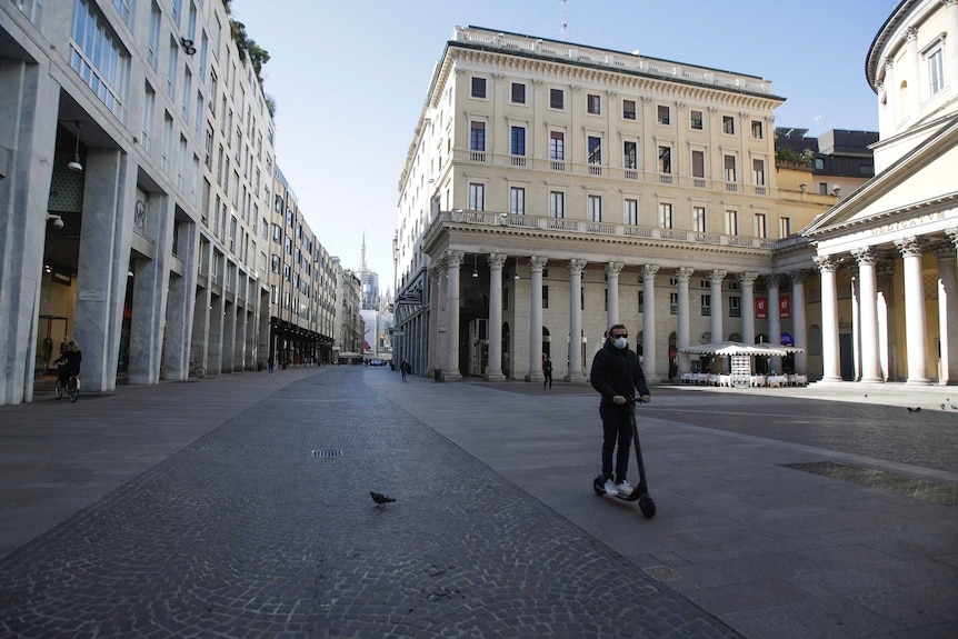 A man wearing a mask rides a scooter through an empty street in Milan.