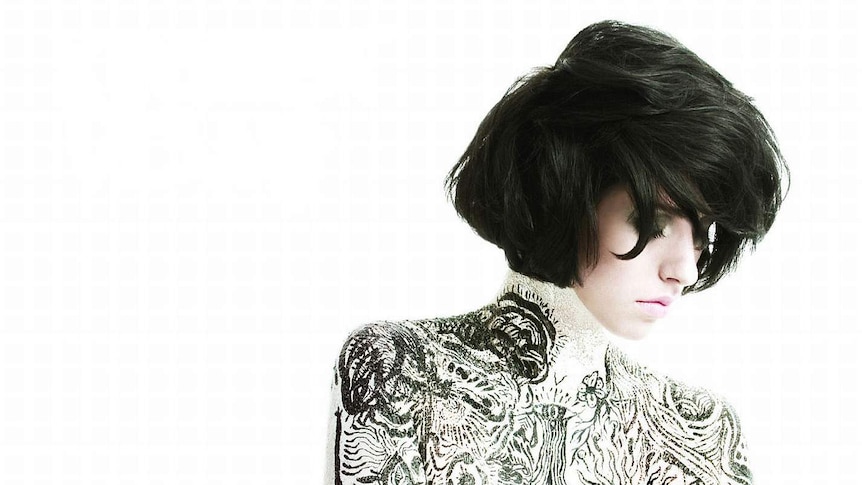 Kimbra, her body covered in intricate painting, against a white background