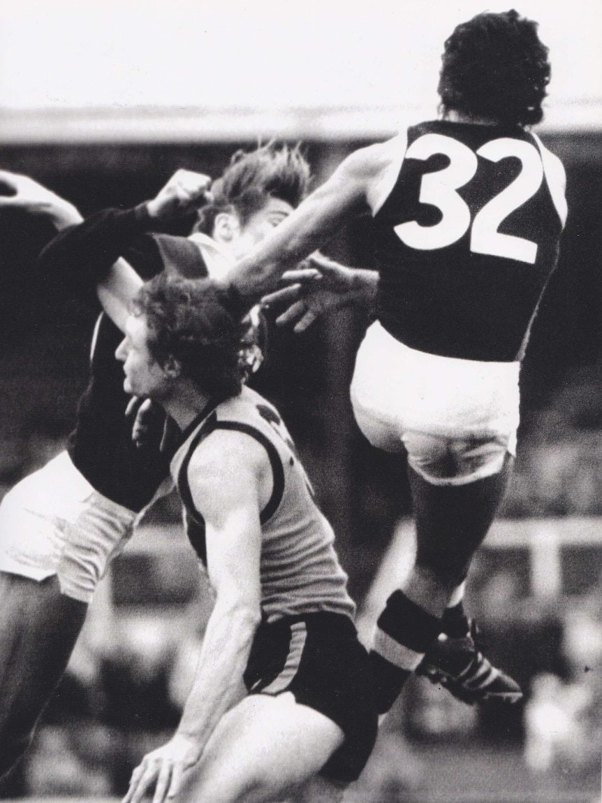 Three VFL players jump and jostle for the ball.
