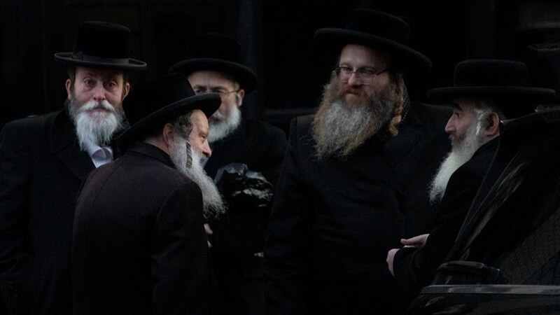 Five orthodox Jewish men against a dark background.
