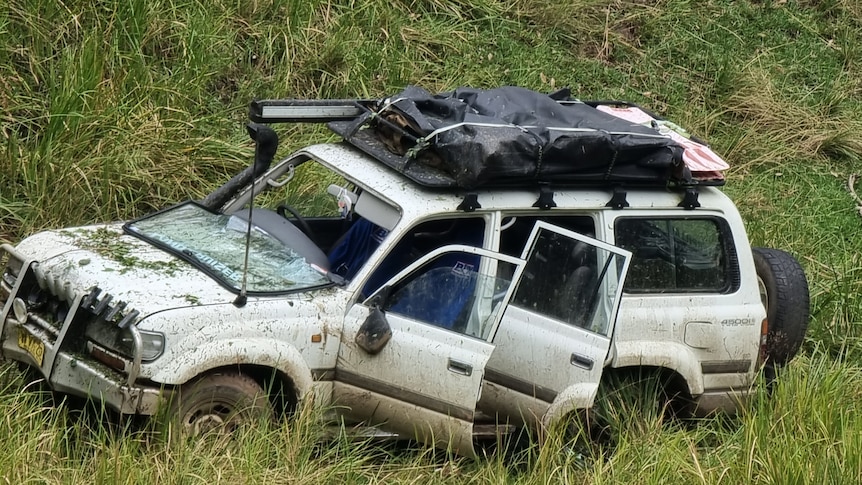 Close up shot of a car covered in grass with damage on the front and two doors open.