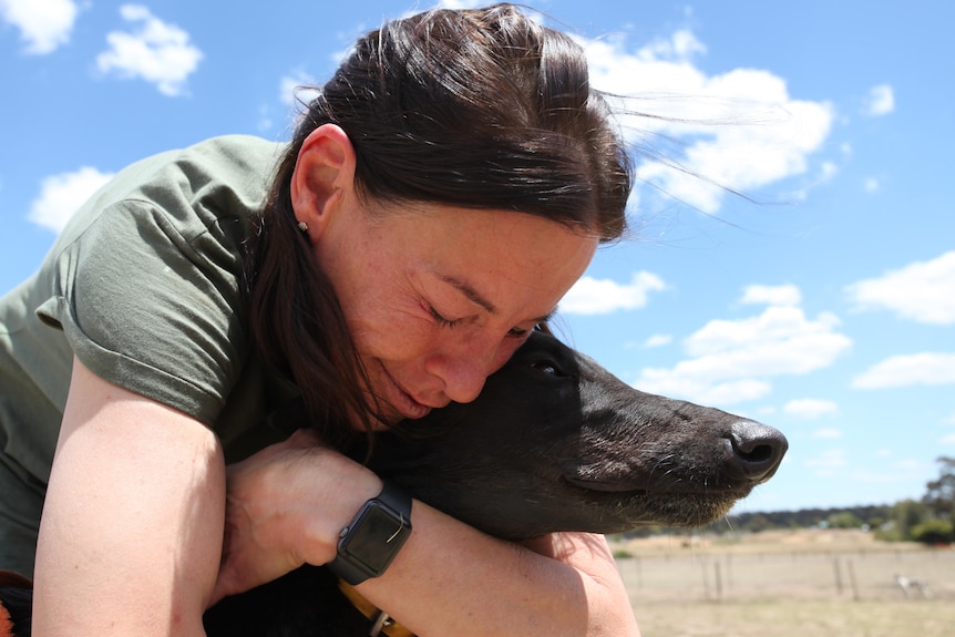 Michele Berry hugs her greyhound while outside on a sunny day.