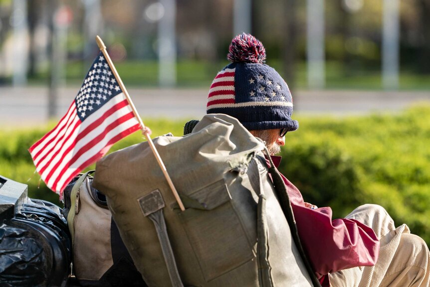 A homeless man with a US flag attached to his backpack