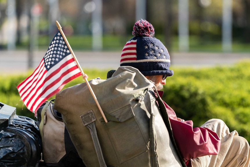 A homeless man with a US flag attached to his backpack