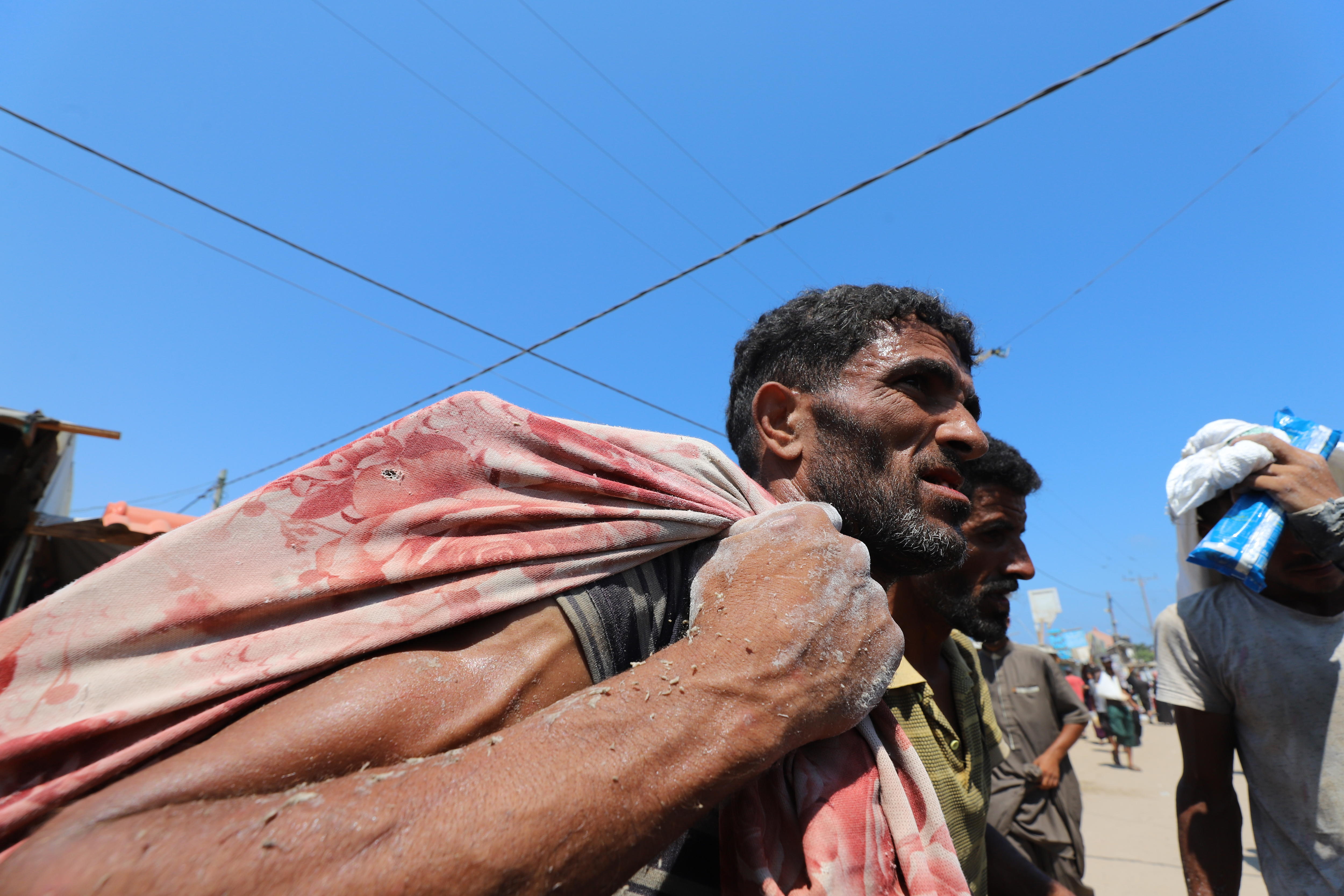 Hassan Abu Obeyd carries a red sack over his right shoulder under a bright blue sky.