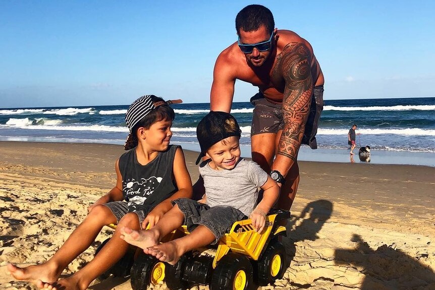 Leroy Faure pushes his two children on a truck toy at a beach on the Sunshine Coast.