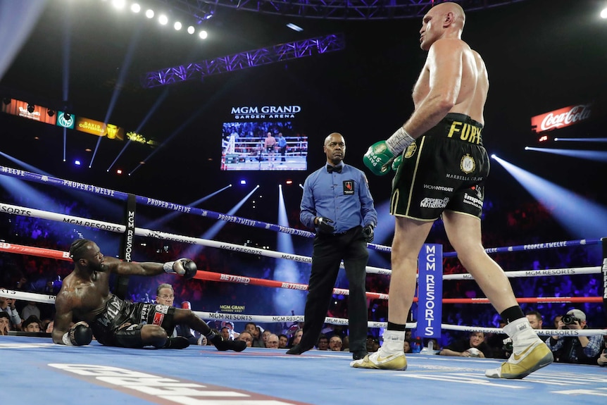 Tyson Fury (right) stands over Deontay Wilder after knocking him down in their heavyweight boxing bout.